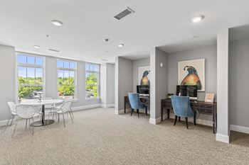 A living room with a table and chairs and a desk and windows